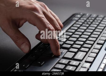 Finger presses the enter button. Typing male hands. Black keyboard button close up, English language and black light keyboard for hacker, gamer, offic Stock Photo