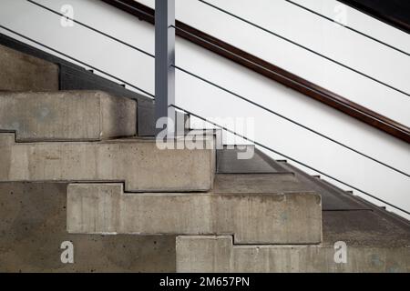 Selective focus at raw concrete riser and tread, and metal railing, loft and brutalist architecture style staircase. Stock Photo