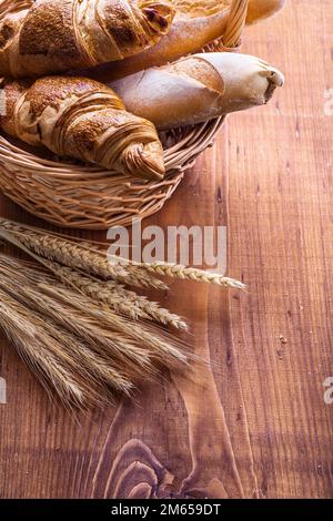 baguettes and croissants in wicker basket with ears of wheat very close up version Stock Photo