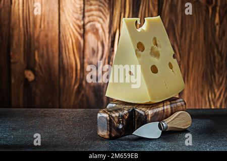 big piece of milk maasdam cheese with knife on little vintage wooden cutting board wooden background Stock Photo