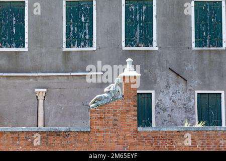 historic marble figure of a beautiful woman at a fence with closed shutter in background at island of Burano, Venice, Italy Stock Photo