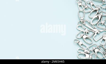 The heap of metal lobster claw clasp for making bags and backpacks lying on a light blue background. Chrome-plated metal accessories and supplies Stock Photo