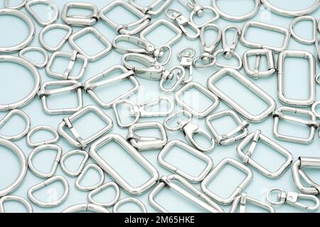 The heap of metal accessories for making bags and backpacks lying on a light blue background. Chrome-plated metal accessories and supplies for bags Stock Photo