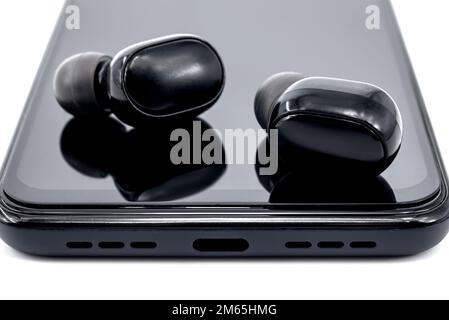 Wireless headphones lie on the surface of a smartphone on a white background. Wireless connection. technologies Stock Photo