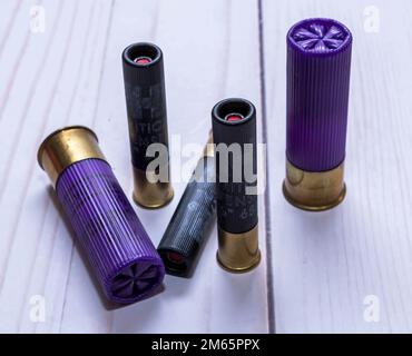 Five Hornady shot gun shells, three black 410 gauge and two purple 12 gauge ones on a white wooden background Stock Photo