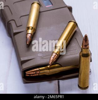 An AR15 rifle magazine loaded with 223 caliber bullets with three additional bullets next to it on a white wooden background Stock Photo