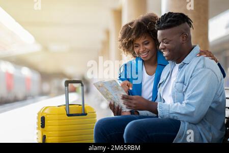 Travelling Together. Happy Black Couple With City Map Sitting At Railway Station Stock Photo