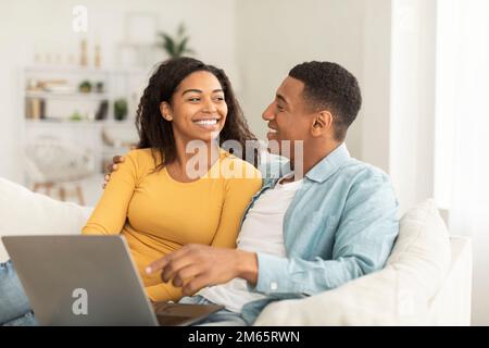 Smiling millennial african american man look at woman use laptop for online call, watch video Stock Photo