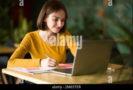 Young businesswoman sitting at table and taking notes in notebook Stock Photo