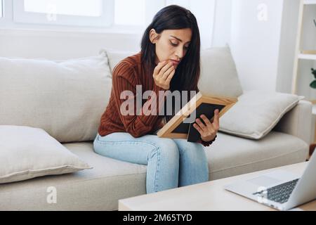 The woman looks sadly at the picture frames in her hands and with memories, a state of depression and loss of a person Stock Photo