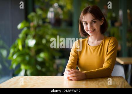 Portrait of beautiful cheerful young brunette woman sitting at cafe Stock Photo