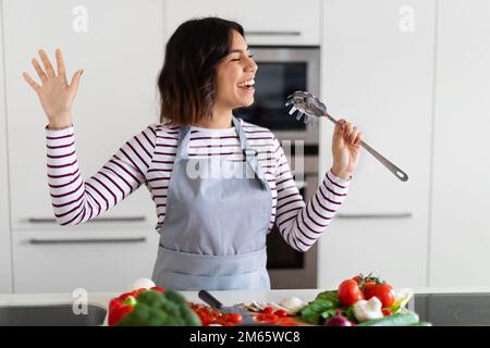 Joyful happy woman singing while cooking in the kitchen Stock Photo