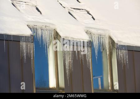 icicles on roof of modern house in sunny winter day. formation of icicles in a thaw. Huge icicles hang down from roof. Ice Dams, Snow on Roof, Icicles Stock Photo