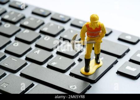 Construction worker figurine with a pickaxe standing on top of a simple desktop PC, computer keyboard. Data mining, crypto, cryptocurrency mining IT s Stock Photo