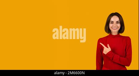 Happy beautiful young lady in red pointing at empty space Stock Photo