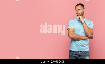 Pensive black man touching his chin, thinking and looking aside at free space on pink studio background, panorama Stock Photo