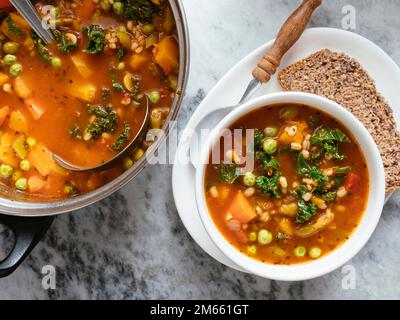 Home made Italian winter minestrone soup with winter squash, carrots, kale, green beans, peas, tomatoes and barley. Stock Photo