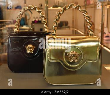 Luxury retail display featuring two Versace La Medusa Patent Mini Bags in black and metallic gold patent leather. The high-shine handbags are adorned with the iconic gold-tone Medusa head plaque and feature fixed chain top handles, showcased in a premium boutique setting. Stock Photo