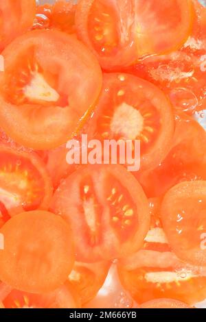 Close-up fresh slices of tomato on white background. Slices of tomato in sparkling water on white background, close-up. Vertical image. Stock Photo