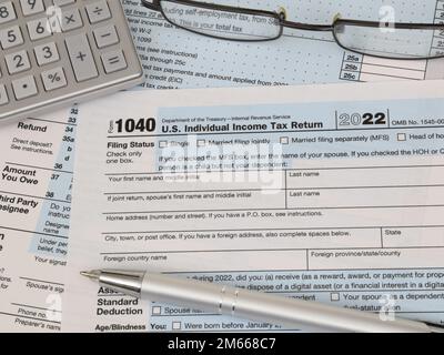 An IRS 1040 tax year 2022 form is shown, along with an ink pen, calculator, and glasses. The 2023 tax filing deadline is April 18. Stock Photo