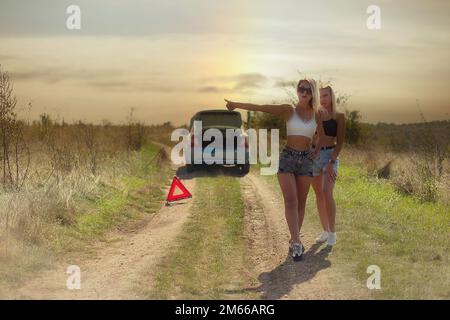 an accident on the road, a car broke down, two beautiful girl models are hitchhiking a car. Showing the thumb up. Problem with the car. Friends waiting for service. In the countryside . High quality photo Stock Photo