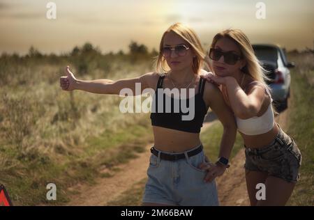 an accident on the road, a car broke down, two beautiful girl models are hitchhiking a car. Showing the thumb up. Problem with the car. Friends waiting for service. In the countryside . High quality photo Stock Photo