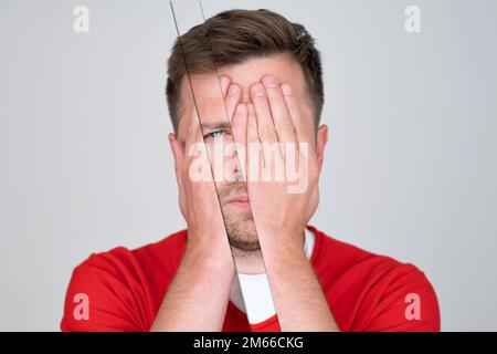 Young man covering his face by hand and looking at camera  Stock Photo