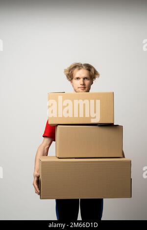 Delivery man in red uniform hold blank cardboard, percel isolated on white background, studio portrait. Male employee working as courier. Service Stock Photo