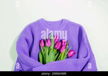 Bouquet of purple tulips wrapped in sweater. International Women's Day, March 8, birthday, Valentine's day concept. Wool sweater hugging flowers. Top Stock Photo
