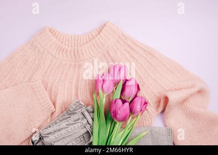 Bouquet of purple tulips on pink sweater and gray jeans. Casual clothes. Spring holidays concept. Top view, flat lay. Stock Photo