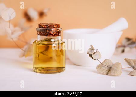 Cosmetic oil in glass bottle, mortar and pestle and eucalyptus branches on white table. Natural cosmetics, skincare, aromatherapy and beauty products. Stock Photo