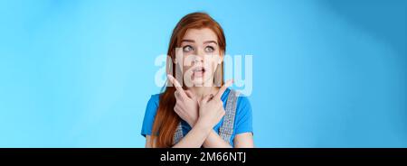 Uncertain cute redhead female making decision, cross arms body, pointing sideways upper left right corners, look aside hesitant, thinking, open mouth Stock Photo