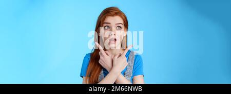 Uncertain cute redhead female making decision, cross arms body, pointing sideways upper left right corners, look aside hesitant, thinking, open mouth Stock Photo