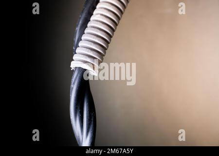 A black power wire enters a plastic gray corrugated tube close-up on a blurred background, a place for copyspace Stock Photo