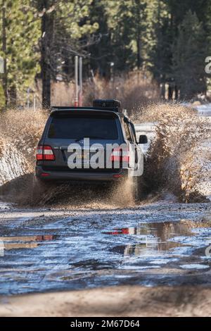 Rear Angle view of Off Road Overland Land Cruiser SUV crossing water on a snowy trail in the forest Stock Photo