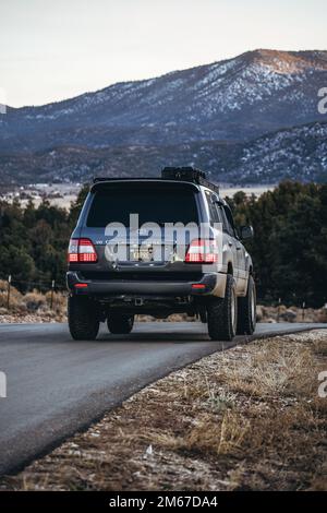 Rear Angle of a Land Cruiser 100 Series SUV overlooking a lake and snowy mountain forest Stock Photo