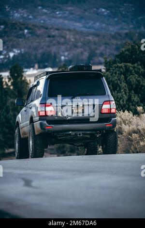 Rear Angle of a Land Cruiser 100 Series SUV overlooking a lake and snowy mountain forest Stock Photo