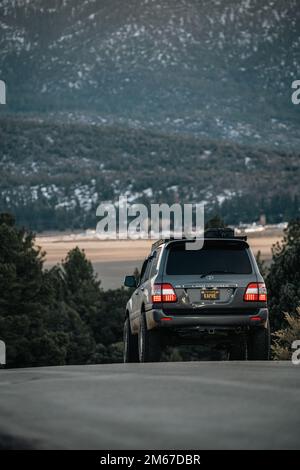 Rear Angle of a Land Cruiser 100 Series SUV overlooking a lake and snowy mountain forest Stock Photo