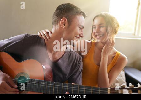 Playing by heart. a young man playing the guitar while relaxing on the sofa with his wife. Stock Photo