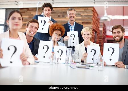 We have the answers to all your questions. Portrait of a group of businesspeople holding up cards with question marks on them. Stock Photo