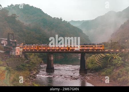 Trains pass over the bridge. The station next to a stream in a foggy valley. Sandiaoling Railway Station, Ruifang District, New Taipei City, Taiwan Stock Photo
