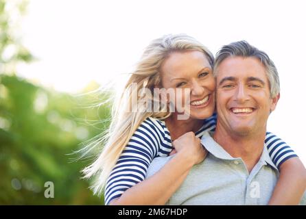 Their love fills the silence. Cropped portrait of a handsome mature man piggybacking his wife in the park. Stock Photo