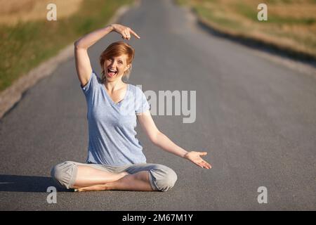 Shes found the road to overall wellbeing. Portrait of a woman looking excited while sitting in the lotus position on a country road. Stock Photo