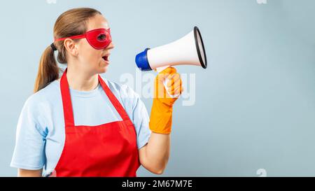 Woman in red mask, gloves and apron with megaphone on blue background Stock Photo