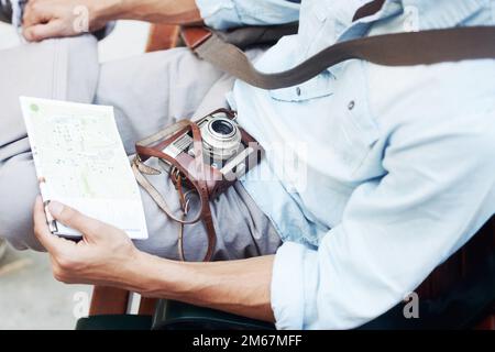 Drawing inspiration from relaxation. Closeup cropped image of a young male resting a map and camera on his lap. Stock Photo