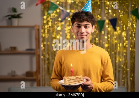 Young handsome man holding birthday sweet cake over golden home background with a happy face standing and smiling with a confident smile. Stock Photo