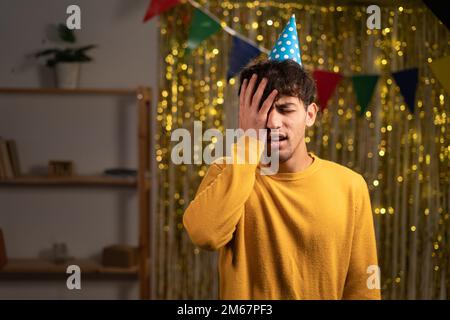 Negative facial human emotions, body language and life perception. Birthday man with cone hat confused, feeling unhappy while realizing that he is Stock Photo