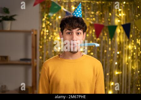 Unhappy birthday guy feeling sad and disappointed, nobody came to celebrate his anniversary, blowing party horn all alone. People and celebration Stock Photo