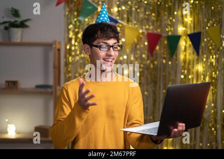 Virtual Party. Happy arabic man in hat having video conference online meeting with friends and family, celebrating birthday at home Stock Photo
