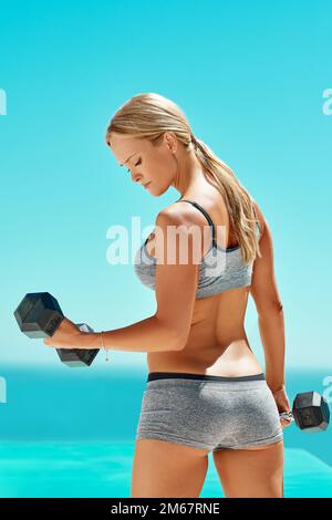 A strong mind and a healthy body. Rearview shot of an attractive young woman exercising with dumbbells outside. Stock Photo
